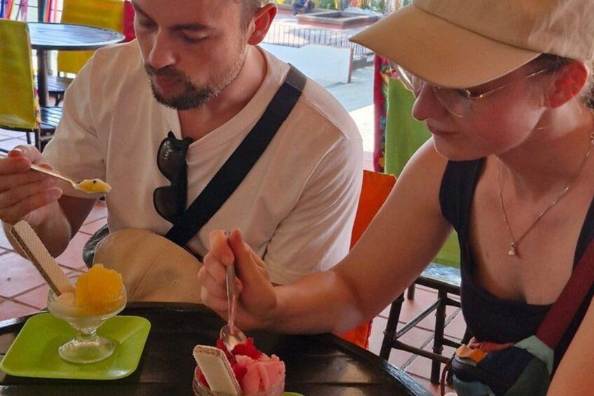 Two people dining at an outdoor restaurant with a green tablecloth, a glass of orange juice, and a dessert. 3