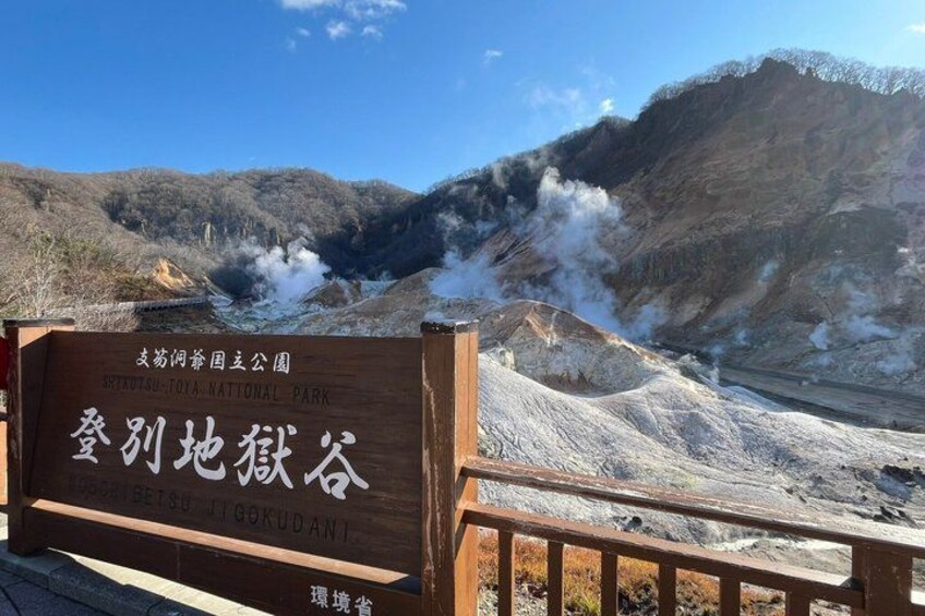A wooden sign with Japanese characters, a mountainous landscape, and steam rising from the ground. 2