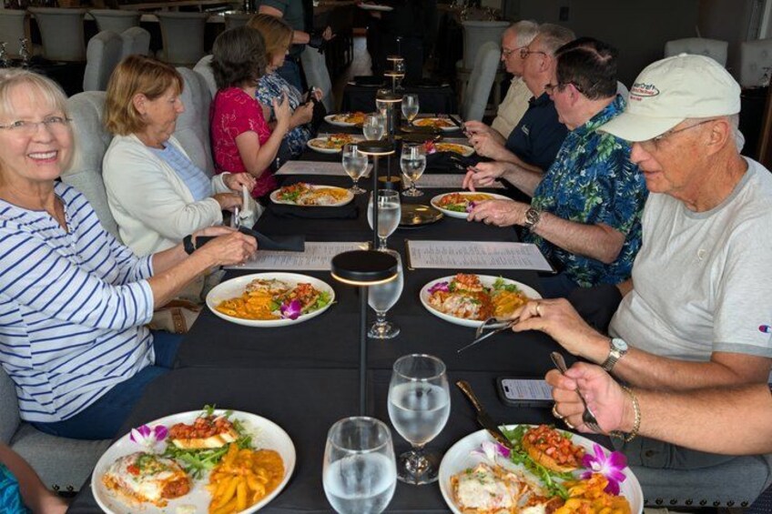A group of people dining at a table with plates of food and wine glasses. 3