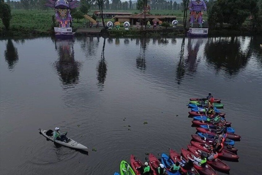 A calm lake with a row of colorful canoes docked on the shore and a statue in the background. 1