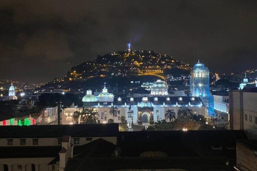 A cityscape at night with illuminated buildings and a hilltop structure. 5