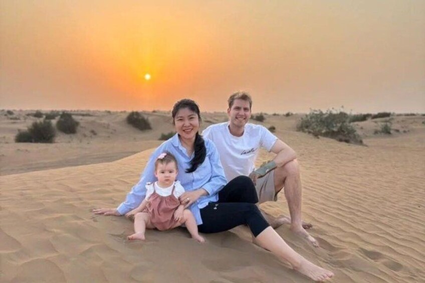 A family of three on a sandy beach with a sunset in the background. 2