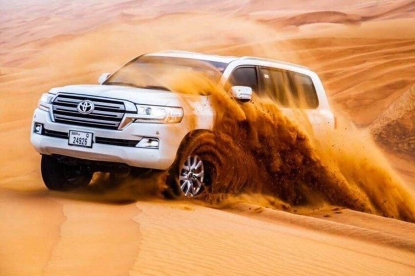 A white SUV driving through a desert with sand being kicked up by its tires. 3
