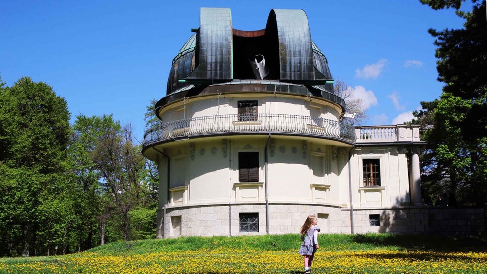 A historic building with a dome and balcony, surrounded by a field of yellow flowers. 1