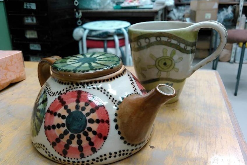 A ceramic teapot and mug with colorful patterns on a wooden table. 3