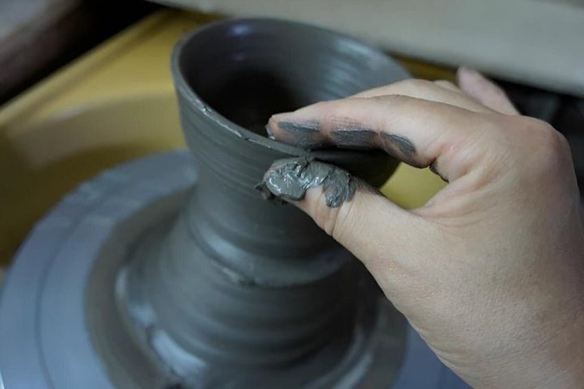 A hand shaping a gray clay pot on a pottery wheel. 4