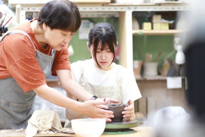 Two people engaged in a pottery activity, with a bowl and a pot on the table. 1