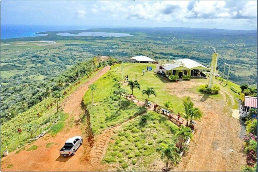 A white vehicle on a dirt road, a building with a white roof, and a landscape with greenery and a distant body of water. 5