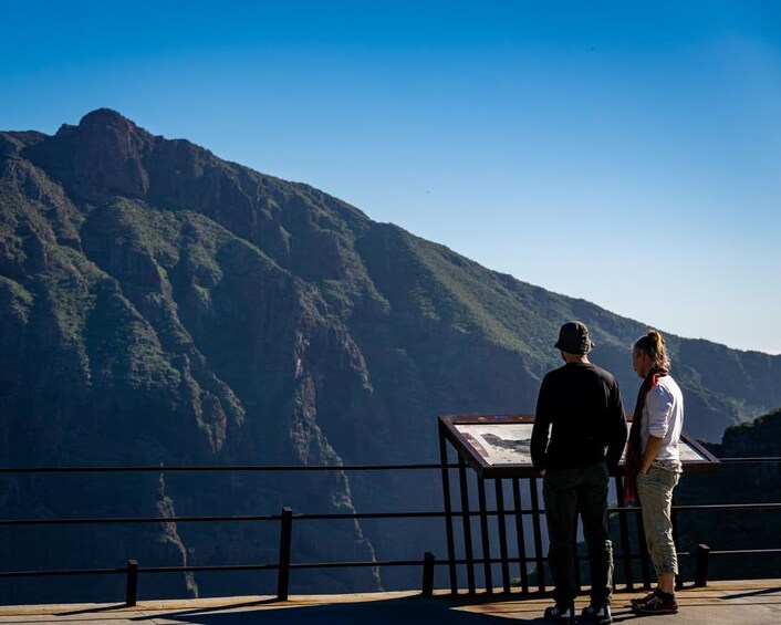 Dos personas de pie en una plataforma de observación con vistas a un paisaje montañoso. 3