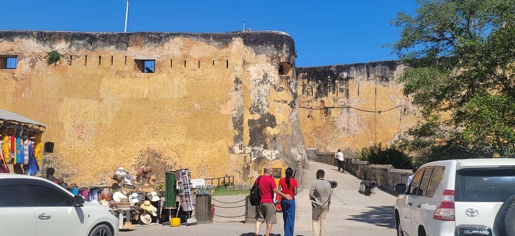 A historic fort with tourists, a market, and parked cars. 4