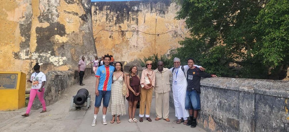 A group of people standing on a bridge with a weathered wall in the background. 1