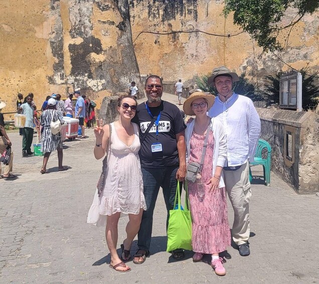 A group of people standing in front of a weathered wall with peeling paint, a green plastic chair, and a metal railing. 3