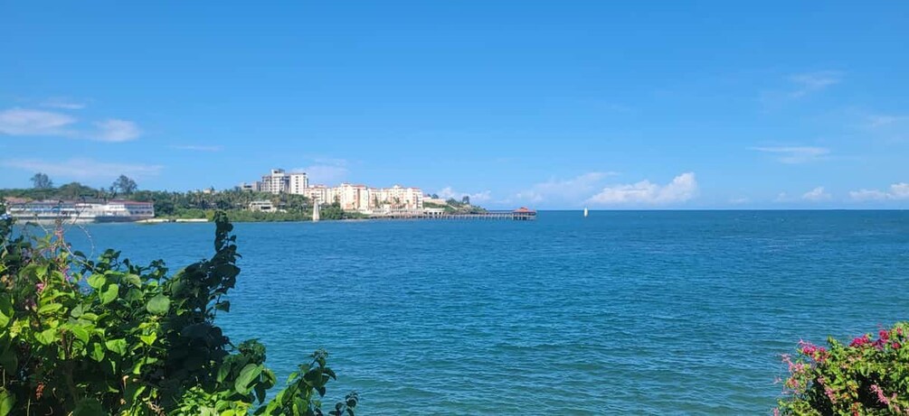 A coastal cityscape with buildings, a pier, and calm blue waters. 2