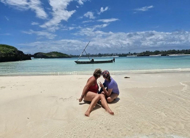 Deux personnes assises sur une plage de sable, avec un bateau en arrière-plan. 5