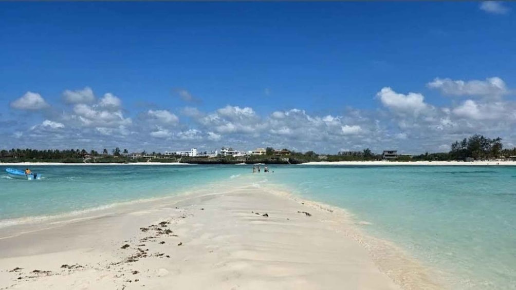 Une plage à l’eau turquoise et limpide, un rivage sablonneux et, au loin, une côte bordée de bâtiments et d’arbres. 2