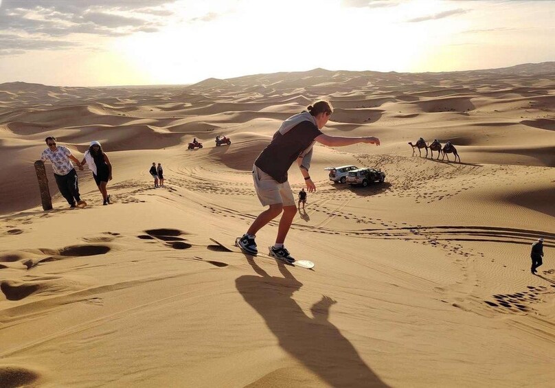 Une personne conduisant un buggy sur une dune dans un désert, avec d'autres dunes de sable et un véhicule en arrière-plan. 3