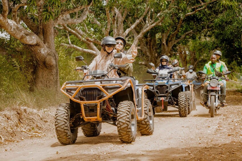 Un groupe de personnes circule en quads sur un chemin de terre, entouré d’arbres. 1