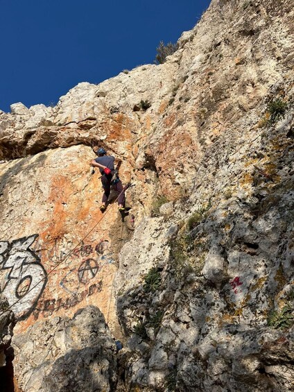 Una persona escala un risco rocoso con grafitis en la pared. 2