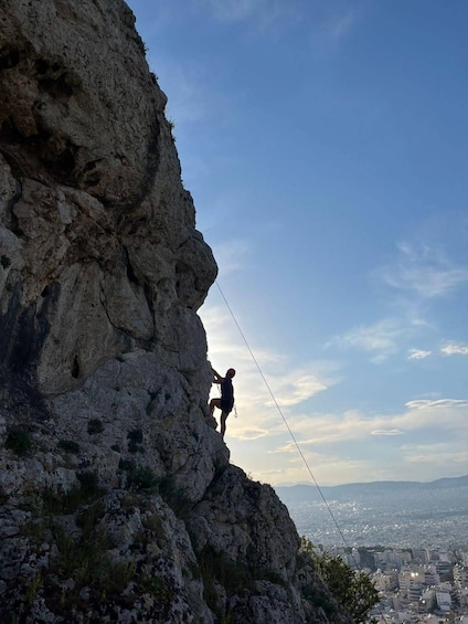 Una persona escalando una pared de roca empinada, con un paisaje urbano de fondo. 3