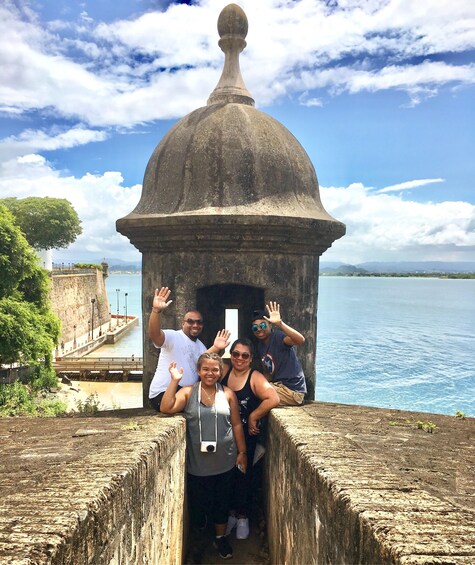 Un groupe de personnes pose devant une structure en pierre d’époque, surmontée d’un dôme, qui surplombe une étendue d’eau et une côte lointaine. 2