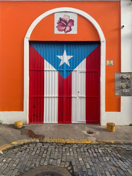 Un bâtiment doté d’une grande porte peinte aux couleurs du drapeau de Porto Rico, d’une arche blanche au-dessus de la porte et d’une petite enseigne ornée d’un visage souriant. 3