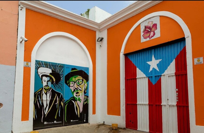 Un bâtiment aux murs orange, doté de deux portes en arc de cercle et orné d’une fresque représentant deux hommes. 1