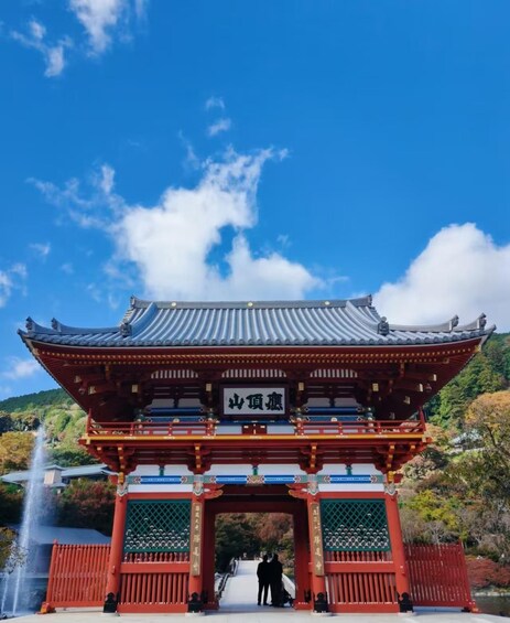 A traditional Japanese gate with a tiled roof and red pillars, set against a clear blue sky with a few clouds. 3