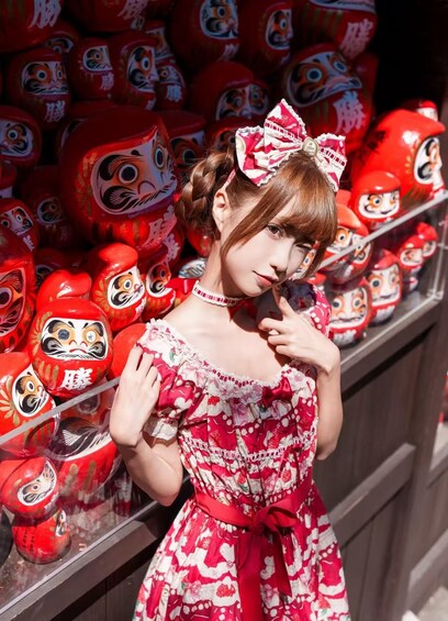 A person in a patterned dress with a bow, standing in front of a display of red lion dance masks. 1