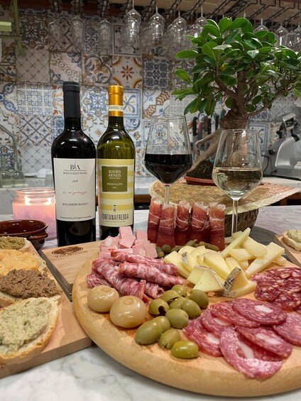 A charcuterie board with various meats, cheeses, and olives, accompanied by bottles of wine and a candle. 1