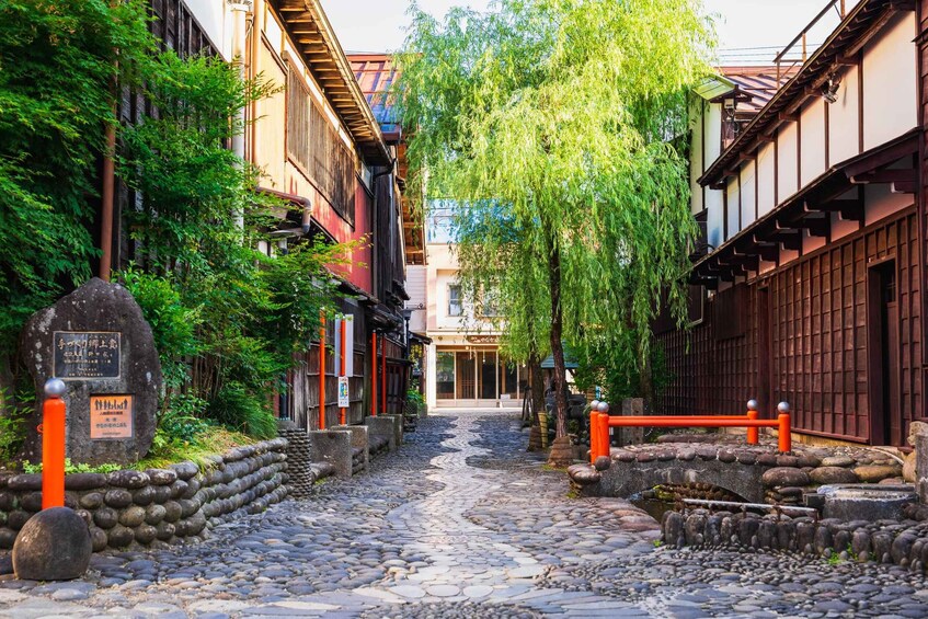 Une ruelle étroite pavée, bordée de bâtiments traditionnels en bois, d’un monument en pierre et d’un saule pleureur. 4