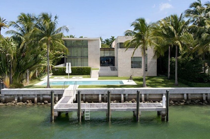 A modern house with a pool, palm trees, and a dock extending into the water. 2