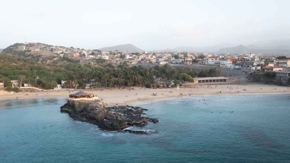 Une ville côtière avec un promontoire rocheux au premier plan, une plage de sable et un quartier résidentiel densément bâti en arrière-plan. 4
