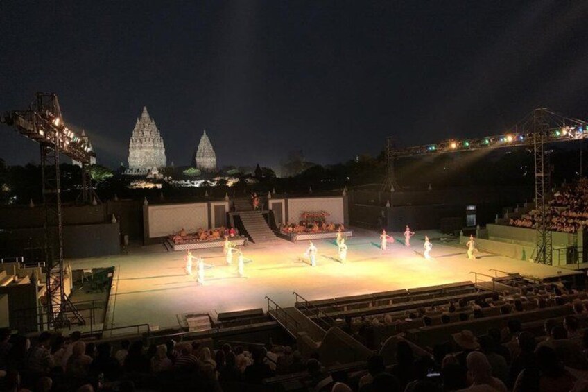 A nighttime outdoor performance with a stage, audience, and illuminated temple in the background. 2