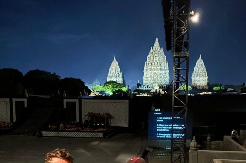 A large illuminated temple complex at night with a stage and a screen displaying text. 5