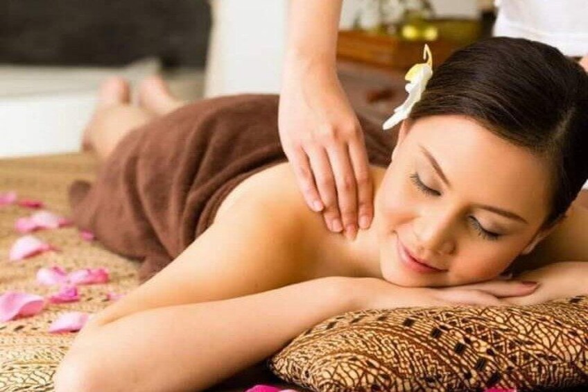 A person receiving a massage on a bed with rose petals scattered around. 4