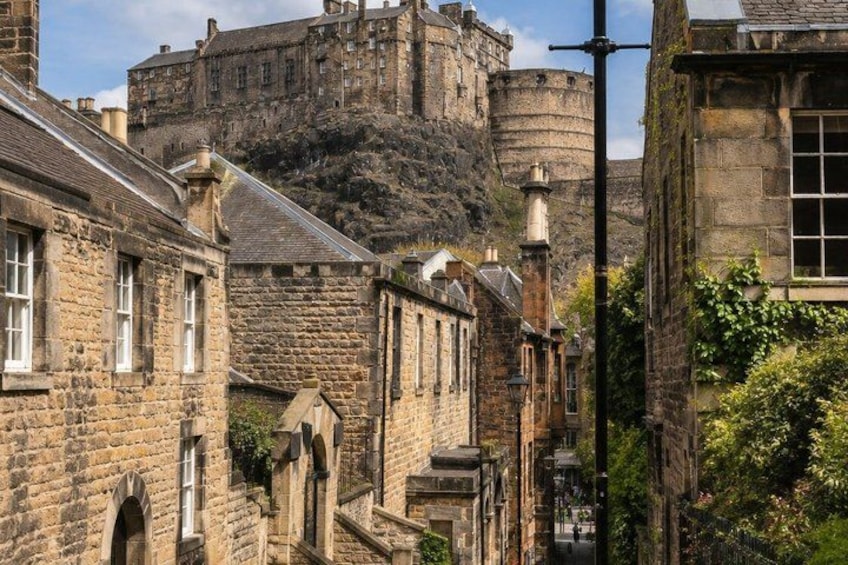 A historic stone building with arched windows, a cobblestone street, and a castle in the background. 3