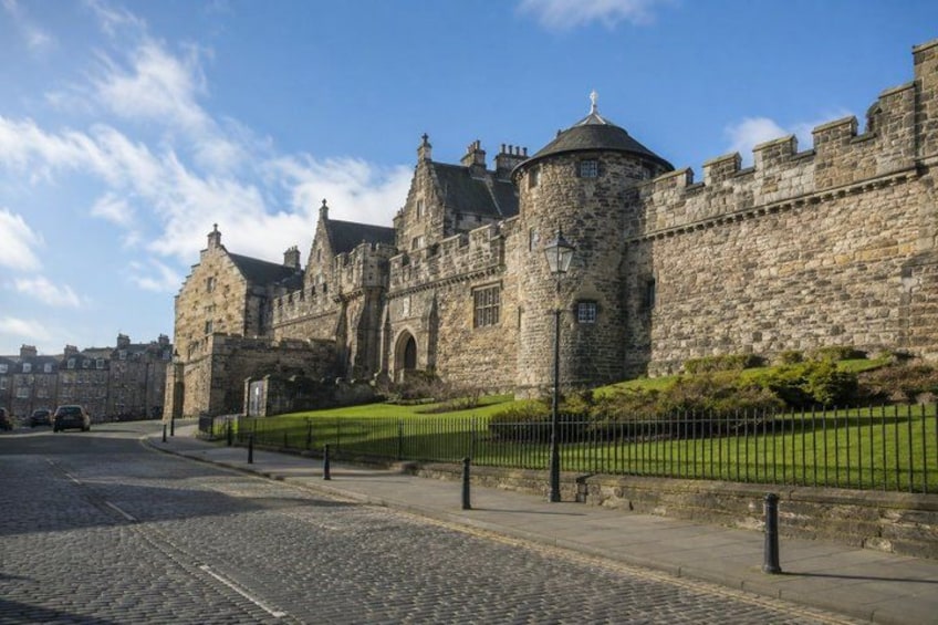 A historic stone castle with a round tower, a paved street, and a green lawn. 5