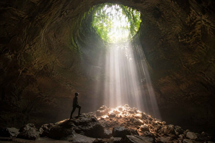 A person standing on a rock formation inside a cave with a natural light source above. 1
