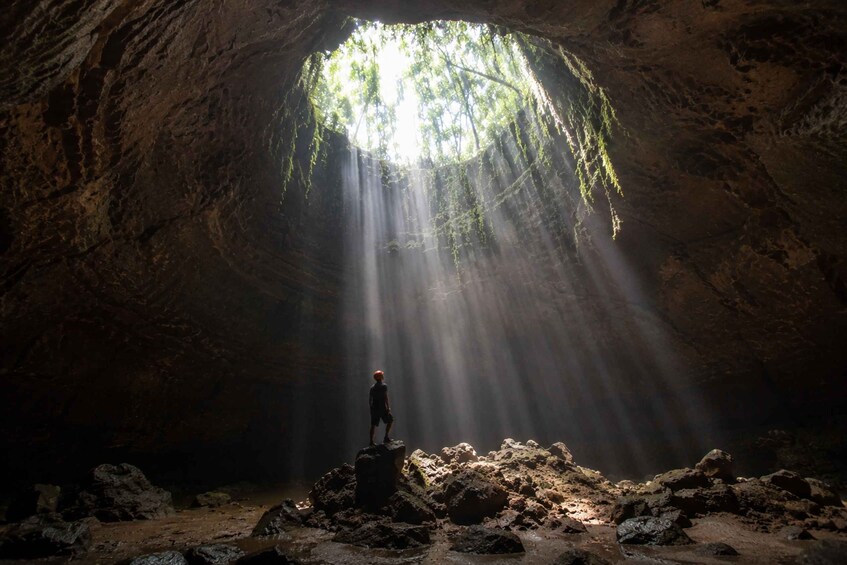 A person standing on a rock formation inside a cave with sunlight streaming through an opening above. 4