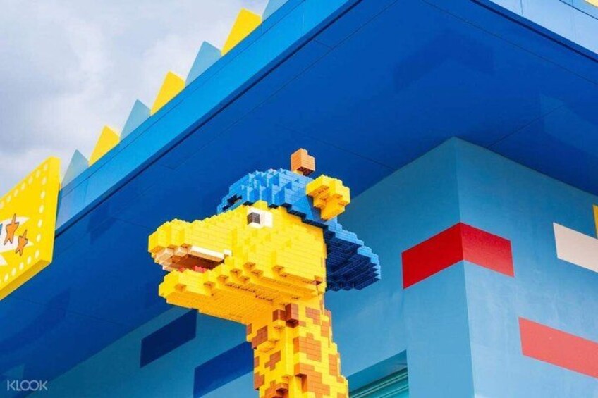 A LEGO giraffe with a blue hat in front of a building with blue and red accents. 5