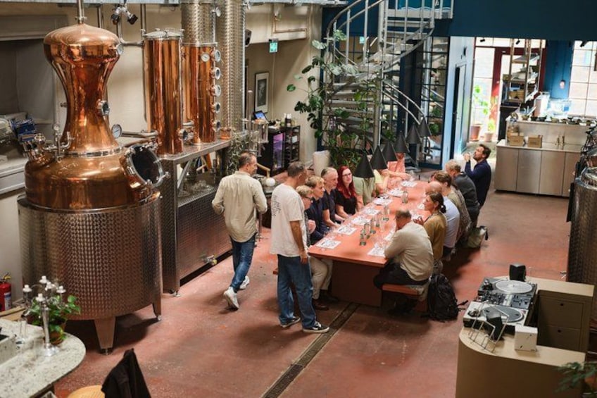 A group of people gathered around a table in a kitchen with copper distillation equipment. 5