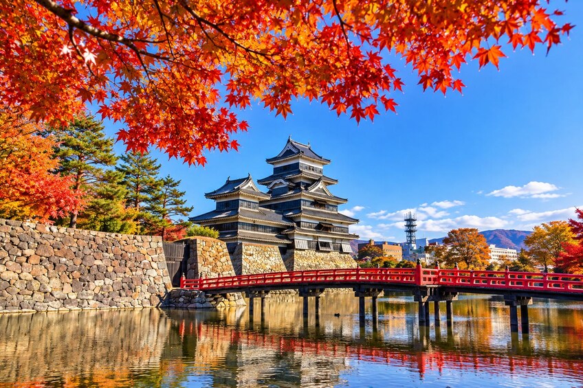 Un castillo japonés tradicional con un muro de piedra y un puente rojo sobre una superficie acuática reflectante. 1