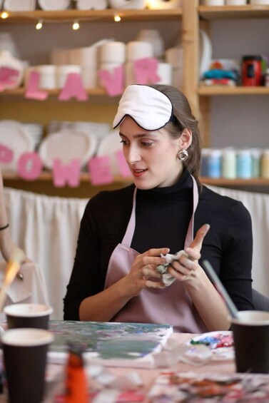 Une personne portant une casquette blanche et un tablier rose, travaillant à une table avec de la peinture et des pinceaux. 4