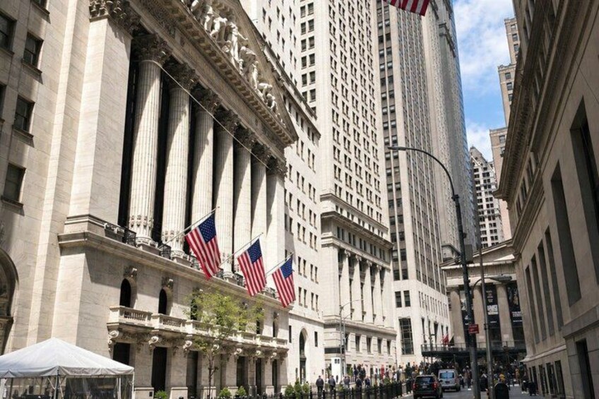 A historic building with columns and American flags, surrounded by tall buildings and a busy street. 5
