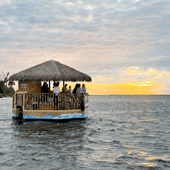 A wooden boat with a thatched roof, people on board, and a sunset in the background. 1