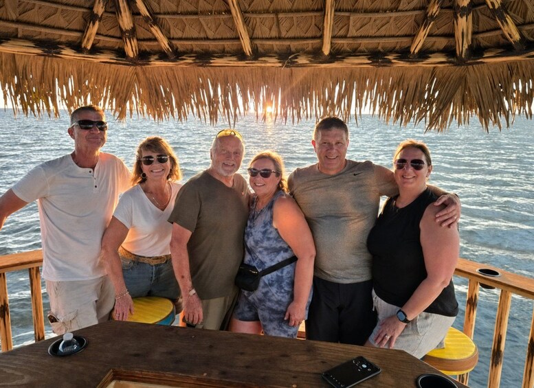 A group of people on a boat with a thatched roof, wooden deck, and a view of the ocean. 4