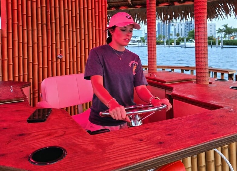 A person operating a boat in a tropical setting with bamboo structures and palm trees in the background. 2