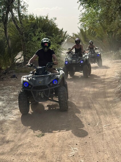Three people riding ATVs on a dirt road surrounded by trees. 5