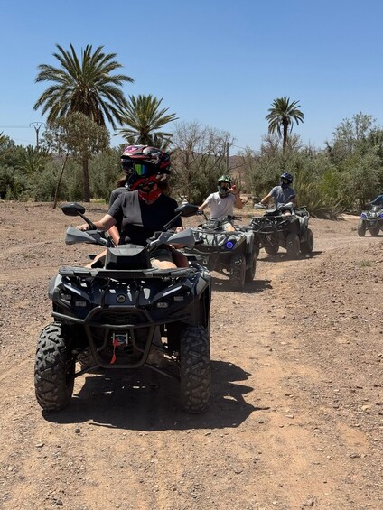 Three people riding ATVs on a dirt path with palm trees in the background. 4
