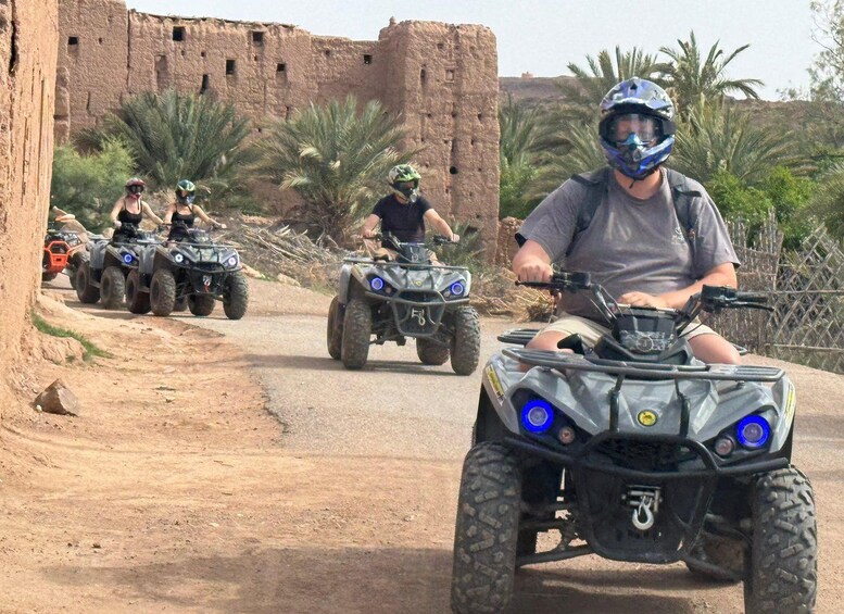 A group of people riding ATVs on a dirt road with a historical building in the background. 1
